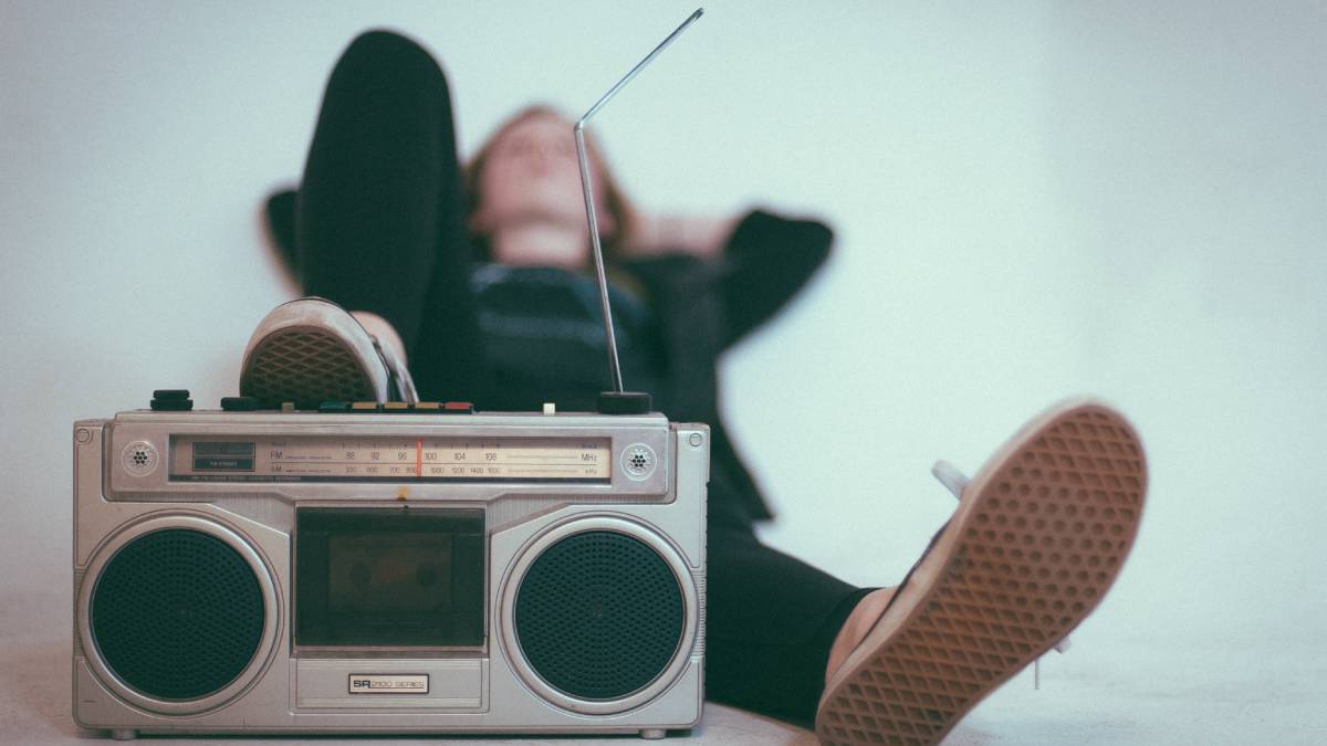 A photo of an old school radio with a bent antenna and a young person resting their foot on the radio